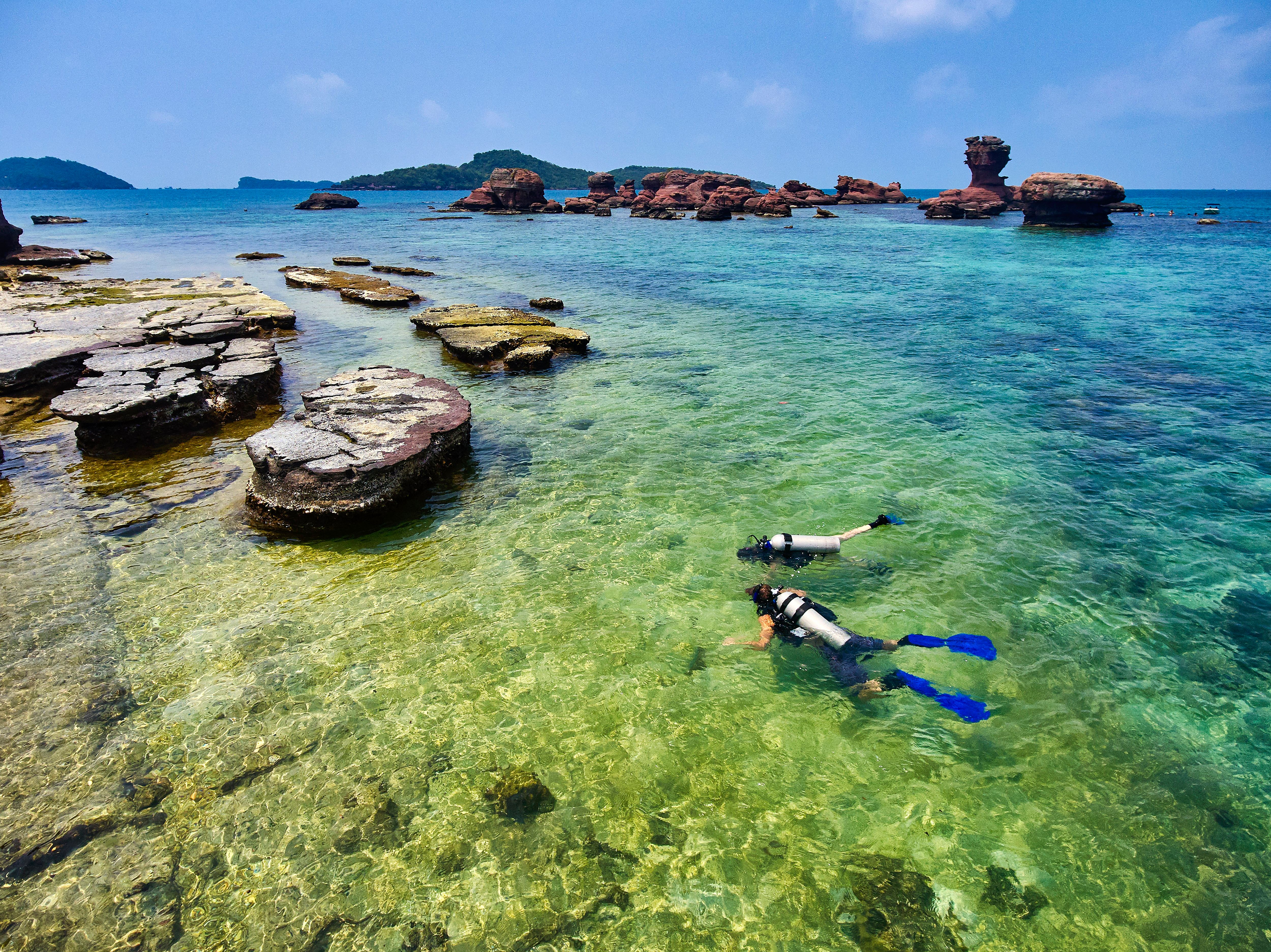 Divers swimming among rocks in clear water on Hom Gam Ghi in Phu Quoc