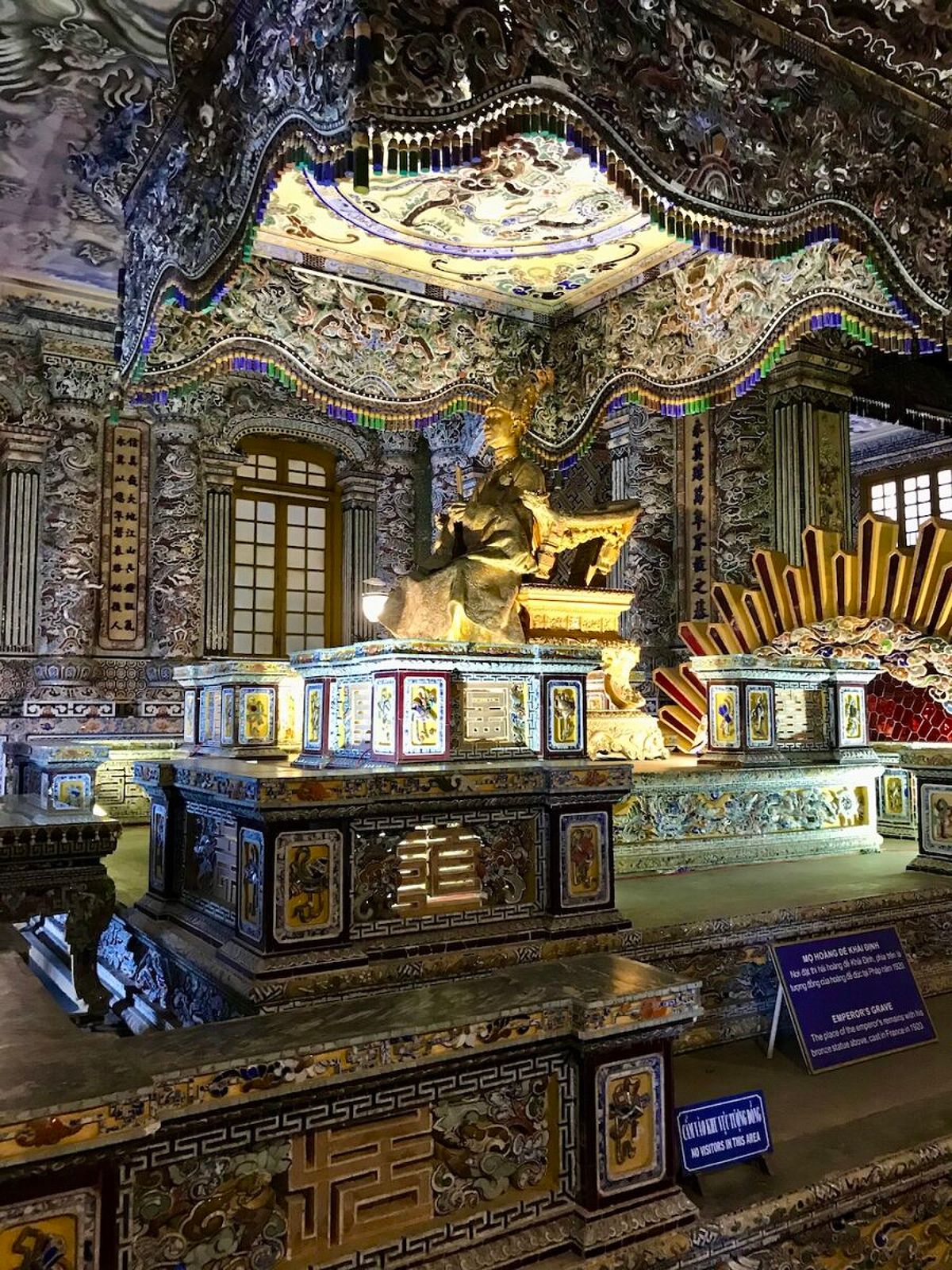 The golden statue of Emperor Khai Dinh is seated under a multicoloured tiled canopy in Hue